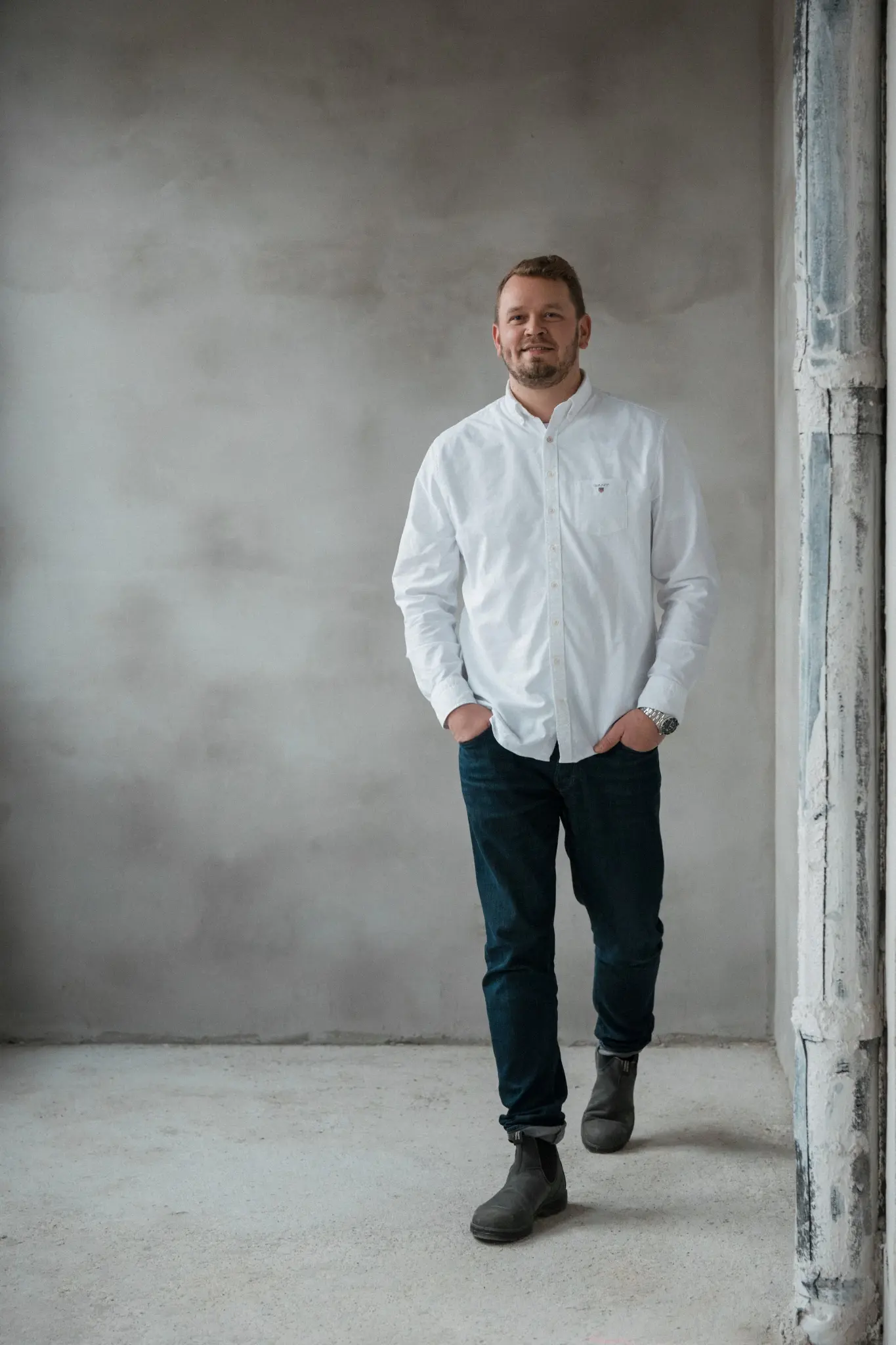 Linus Bocklage von B + B Architekten steht vollständig vor einer grauen Wand in einem hellen Innenraum.